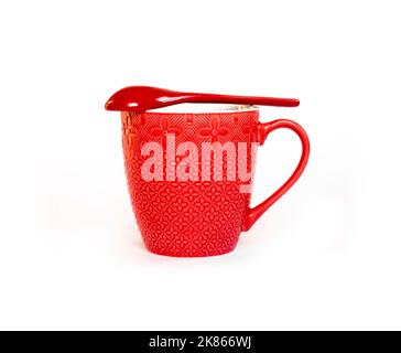 Red ceramic mug with red ceramic spoon lying over it isolated on white background Stock Photo