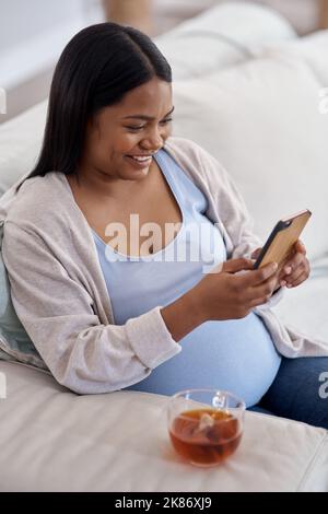 This app is great for expecting moms. a pregnant woman using her cellphone while sitting at home. Stock Photo