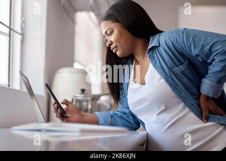 I just finished my last project before officially going on maternity leave. a pregnant woman using her cellphone while sitting at home with her laptop Stock Photo