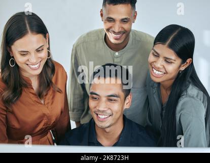 Creating is our speciality. a diverse group of businesspeople standing together in the office and using a computer. Stock Photo