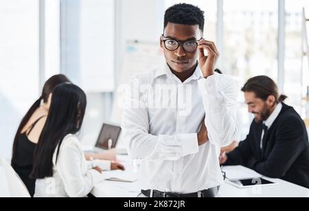 He doesnt mess around. Portrait of a young businessman standing in an office with his colleagues in the background. Stock Photo