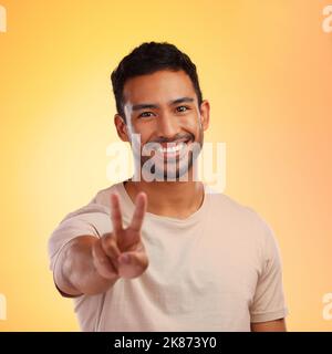 Happiness and peace, those two things matter the most to me. a young man showing the peace sign while standing against a yellow background. Stock Photo