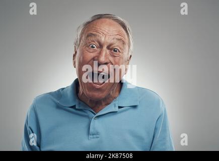 Really that sounds amazing. an older man making an excited expression at the camera in a studio against a grey background. Stock Photo