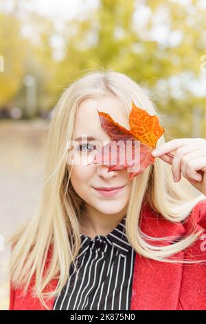 A young blonde woman walks around the autumn city in a red coat. The concept of urban style and lifestyle. Stock Photo