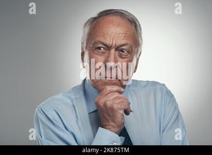 Hmm, some big last minute plans. a senior businessman standing alone against a grey background in the studio and looking contemplative. Stock Photo