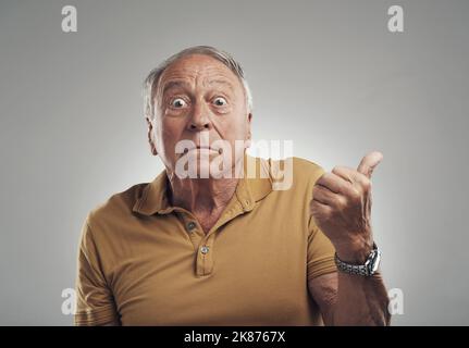 He did it...Studio shot of an elderly man pointing in at something against a grey background. Stock Photo