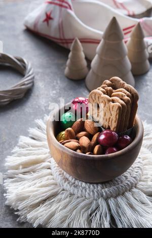 Speculoos or Spekulatius, Christmas biscuits, chocolate balls and almonds in wooden bowl. Winter snacks on a table with wooden Xmas tree toys Stock Photo