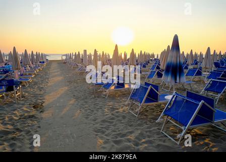 sun umbrellas and sun beds on the beach across sunrise sky. Pathway on the sand to the beach. Summer vacation background. Senigallia, Italy Stock Photo