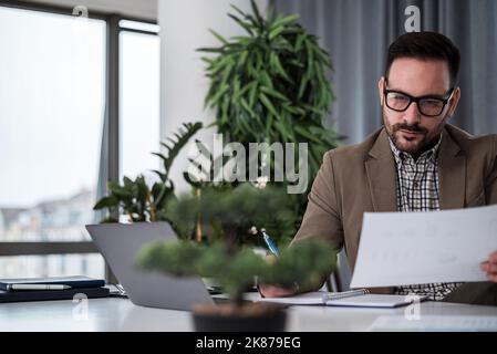 Concentrated adult man with eyeglasses, checking the company files, taking notes. Stock Photo