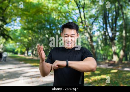 Sport Caucasian man looking smart watch at modern track runner using use smartwatch fitness bracelet Portrait fit male athlete checking result jogging in sportswear in street urban city park outdoor Stock Photo
