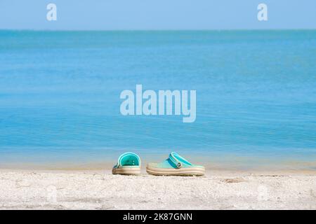 Krasnodar region. Russia. July 19, 2022. A pair of blue Crocs sandals on a sandy beach with a blurred sea background. Beach shoes on the seashore on a sunny summer day. Beach holiday concept. Stock Photo