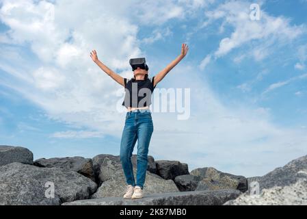 woman wearing a VR headset reaching out to the sky. Stock Photo