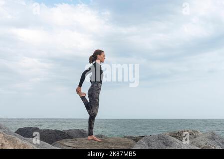 Sporty female doing a leg stretch, warm up exercises by the sea. Stock Photo
