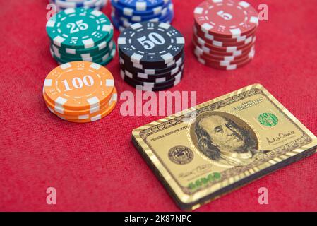 Top view of golden 100 dollar playing cards next to stacks of chips on red felt table. Poker game is one of the most popular card games in the world a Stock Photo