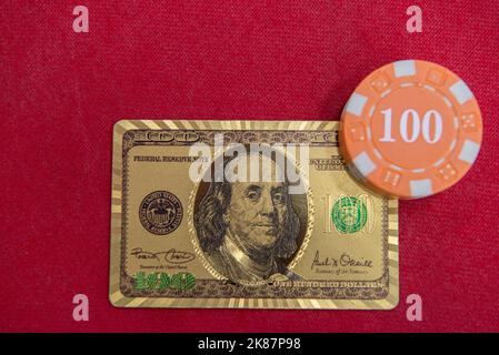 Top view of golden 100 dollar playing cards next to stacks of chips on red felt table. Poker game is one of the most popular card games in the world a Stock Photo