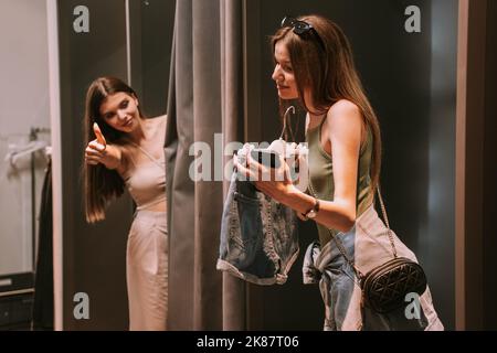 Two pretty best friends standing in the changeing room. One of the showing the shorts the other one liking them Stock Photo