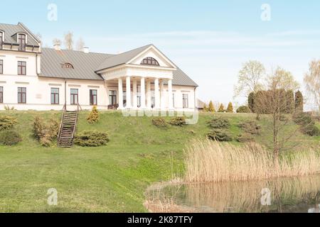 Belarus, village Radzivilki, 01.05.22. Restored old manor Svyatsk Gkursky in Belarus. View to main entrance with columns on bank of small pond with Stock Photo