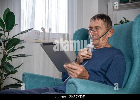 elderly senior sits in a armchair with an oxygen mask and tablet Stock Photo