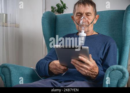 elderly senior sits in a armchair with an oxygen mask and tablet Stock Photo