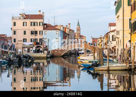 Chioggia cityscape with narrow water canal with moored boats, buildings, brick bridge and tower of San Giacomo Apostolo church – Venetian lagoon,Italy Stock Photo