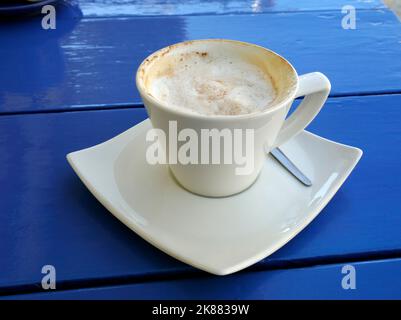 Partially drunk cappuccino coffee in white cup with saucer on a blue table Stock Photo