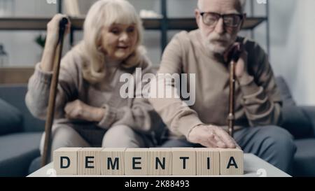 Senior woman sitting near man putting wooden cube with lettering and creating word dementia Stock Photo
