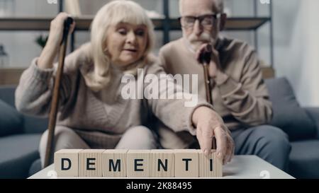Senior man sitting near woman putting wooden cube with lettering and creating word dementia Stock Photo