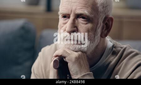 bearded and sad senior man with dementia leaning on walking cane alone Stock Photo