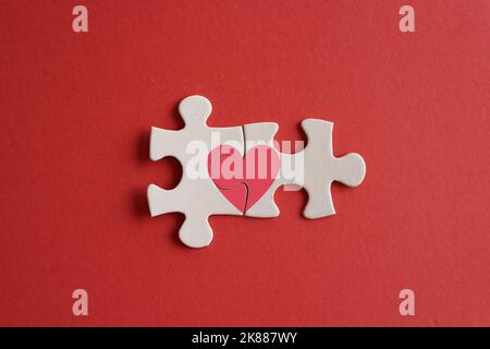 Top view image of connected jigsaw puzzle pieces with red heart icon on red background. Love and relationship concept Stock Photo