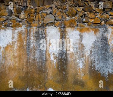 Rock and cement wall with upper portion composed of rocks and lower portion composed of cement, predominant colors are orange color, grey and white, o Stock Photo