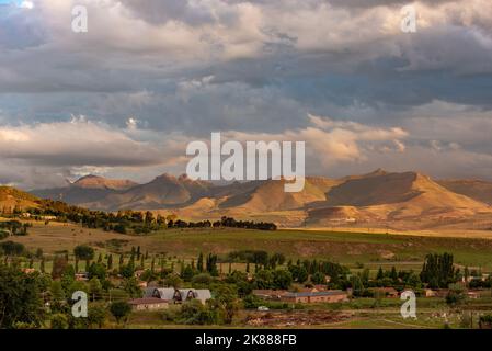 A view of the mountains lit up in gold under a stormy sky at sunset in Clarens, South Africa. This popular tourist destination is near the Golden Gate Stock Photo
