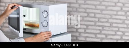 Woman Using Open Microwave Oven. Heating Food Stock Photo