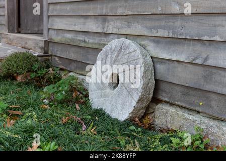 Old vintage mill has a replica millstone grinding stone leaning against the old wood siding of the buidling. Stock Photo
