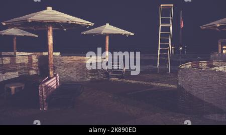 Wooden sun umbrellas, sun beds and windscreens on a beach at night, color toning applied. Stock Photo