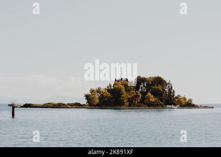 An island in Greece surrounded by blue water on all sides. On an island on a hill, a white house among many trees on which shines a beautiful orange s Stock Photo