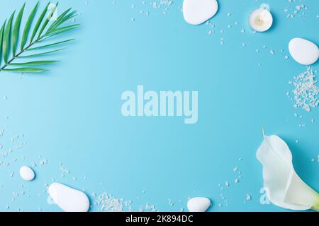 Spa background with white stones, candles, palm leaf and white flower on blue. Flat lay,copy space Stock Photo