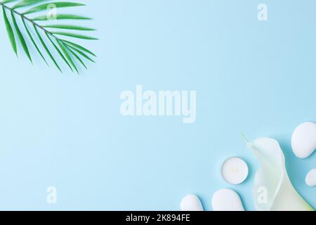 Spa background with white stones, candles, palm leaf and white flower on blue. Flat lay,copy space Stock Photo
