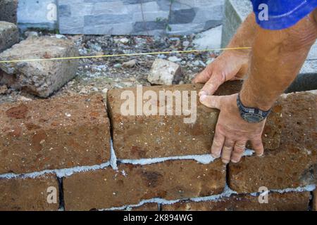 Image of the hands of a bricklayer who builds a wall with tuff bricks following the thread for accuracy. DIY building constructions Stock Photo