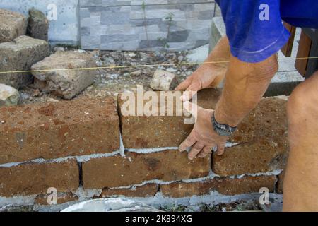 Image of the hands of a bricklayer who builds a wall with tuff bricks ...
