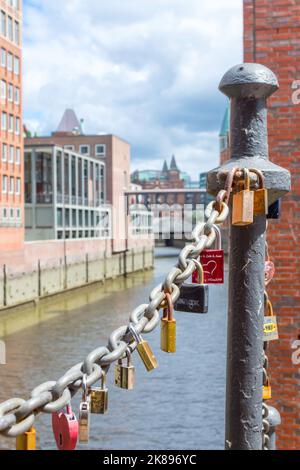 On an old link chain of the Speicherstadt in Hamburg hang many colorful so-called love locks in different shapes. The chain stands out against Stock Photo