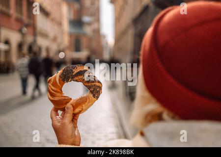 Tourist woman holding bagel prezel obwarzanek traditional polish cuisine snack on Market square in Krakow, Europe  Stock Photo