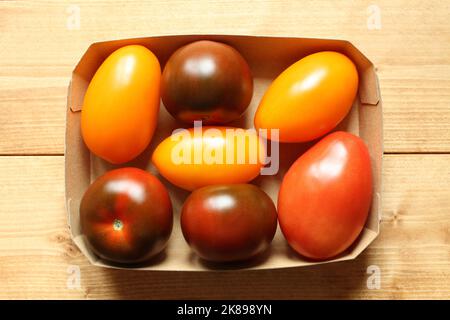 Yellow and red plum tomatoes in a cardboard box on a wooden table. View from above Stock Photo