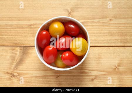 Yellow and red small tomatoes in a cardboard box on a wooden table. View from above Stock Photo