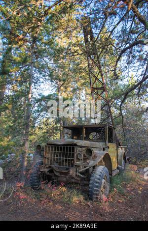 An old rusty abandoned truck sits in the woods in front of a crane. Probably 1940's vintage & used to help build the Alaska Highway. Yukon, Canada Stock Photo