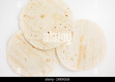 Plain wheat tortilla wraps. Spanish or Mexican circular unleavened flatbread from wheat flour. Ingredient for cooking fast food or snack. Closeup, white background Stock Photo
