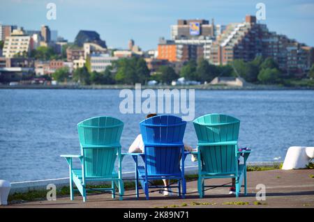 People lounge in colourful seating, Adirondack chairs (Muskoka chairs), on the urban waterfront of the Atlantic Canadian city of Halifax, Nova Scotia Stock Photo