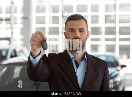 Handsome businessman customer holding key stands near car in dealership center Stock Photo