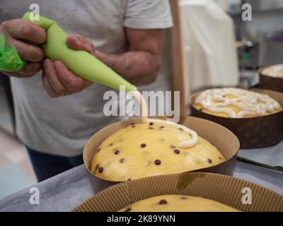 artisan using frosted filling piping bag to decorate a group of cakes Stock Photo