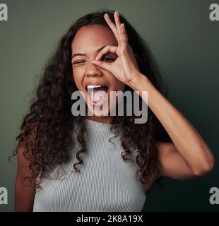 I spy with my beautiful eye. Studio shot of a young woman looking through her fingers against a green background. Stock Photo