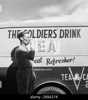 Cecil Beaton - General India 1944: A soldier drinking a cup of tea next to a Red Cross Mobile tea wagon at Calcutta airport. Stock Photo